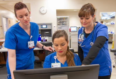Three women in scrubs look at a computer together