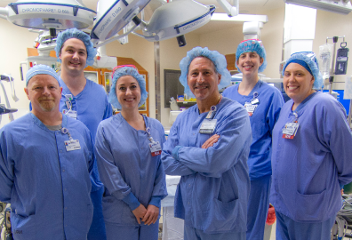 A group of six people in surgical scrubs stand in an operating room